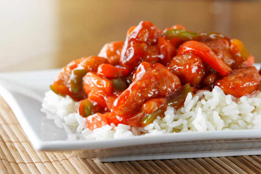 A plate of sweet and sour chicken over a bed of white rice.